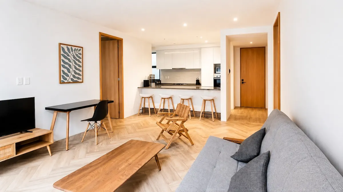 Sala y comedor del departamento, con barra de cocina y bancos al fondo